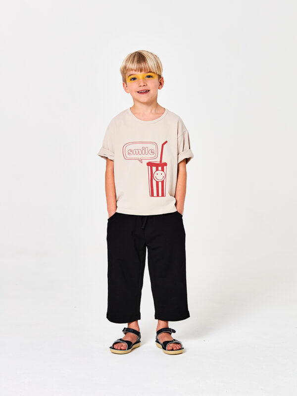 beżowy t-shirt dziecięcy, z krótkim rekawem, koszulka dla dziecka bawełniana z nadrukiem, kremowa, czarne dzianinowe spodnie dziecięce, bermudy, spodnie długość 3/4
